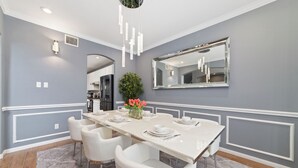 A dining area with a long table, white chairs, and a mirror on the wall. - Spacious Luxury 5BR Home • Game Room • Near Safari Event Center (Sugar Land)