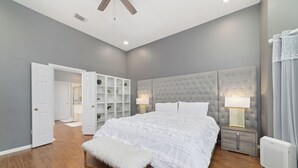 A bedroom with a large bed, a bench, a nightstand with a lamp, a wardrobe, and a radiator. - Spacious Luxury 5BR Home • Game Room • Near Safari Event Center (Sugar Land)