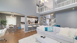 A spacious living area with a white sofa, a dining table, and a kitchen in the background. - Spacious Luxury 5BR Home • Game Room • Near Safari Event Center (Sugar Land)