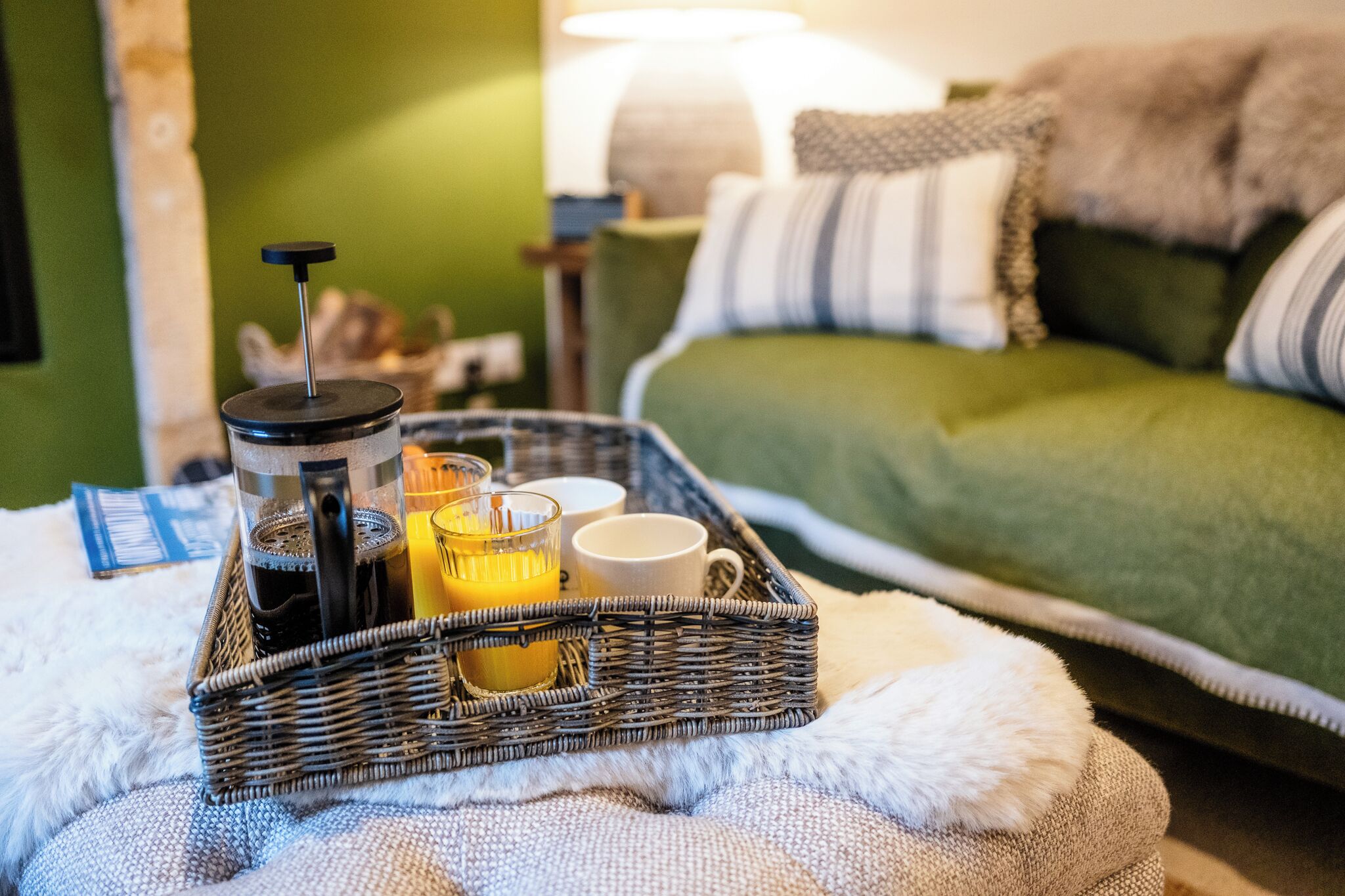 Un plateau en osier avec une cafetière, des verres et une tasse posés sur un coussin blanc et moelleux.