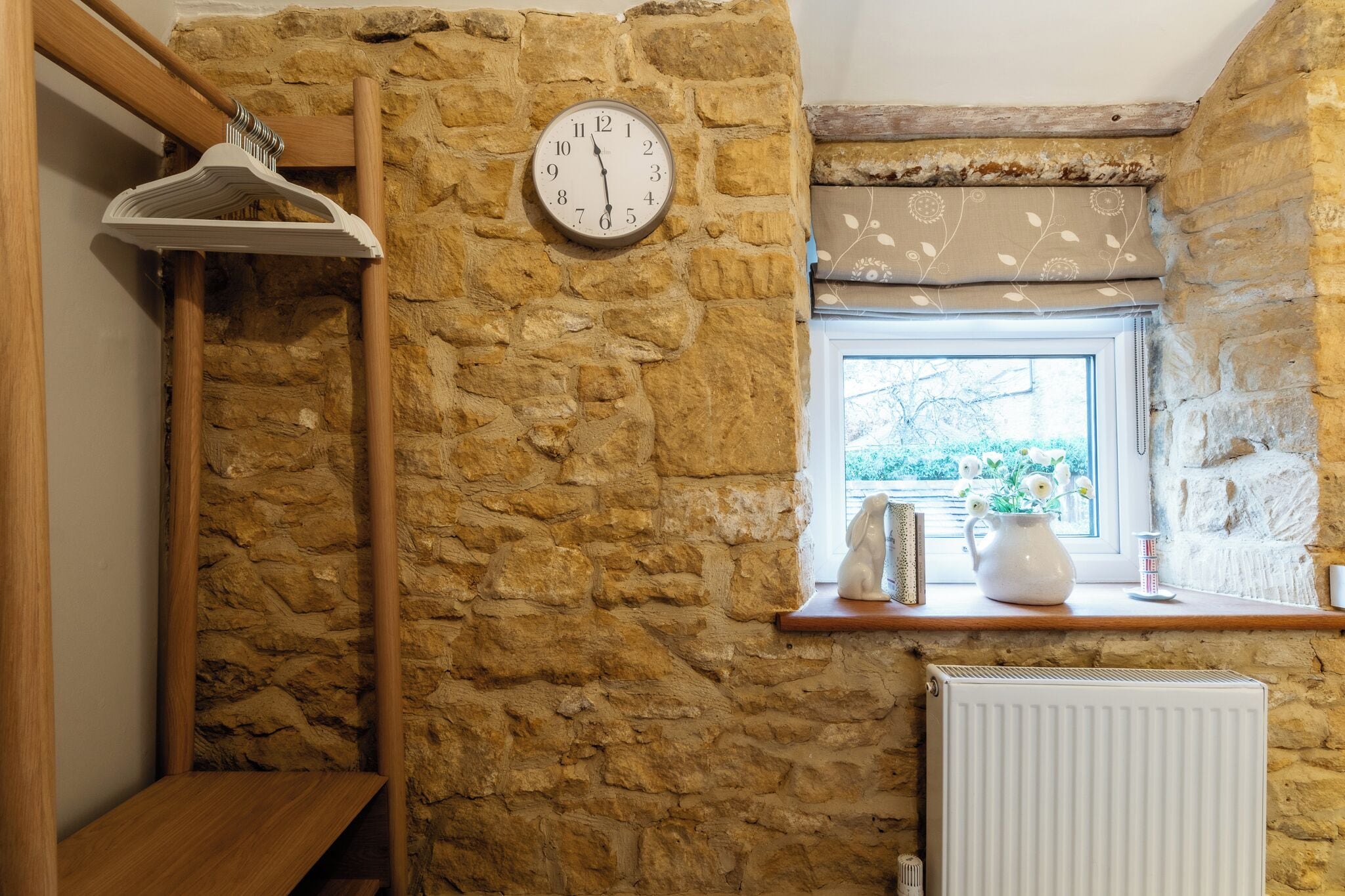 A stone-walled room with a wooden shelf, a white radiator, and a clock.