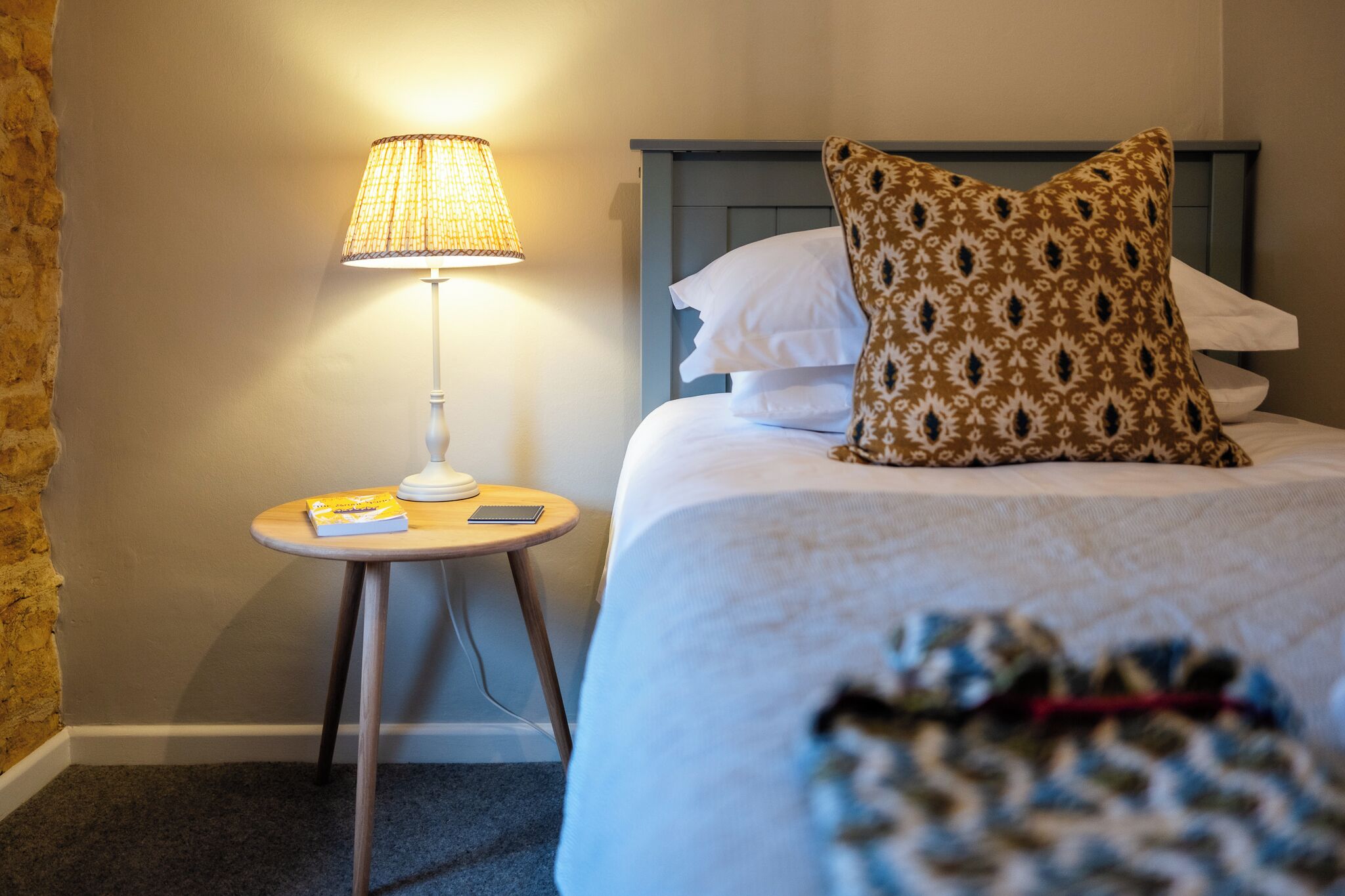 A neatly made bed with a patterned pillow and a bedside lamp on a small wooden table.