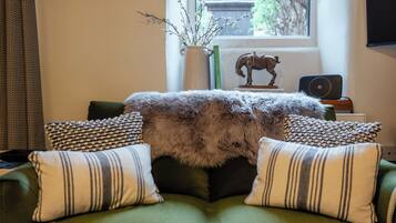 A cozy living room with a green sofa, striped pillows, a fur throw, a small table with a decorative horse statue, a vase with branches, and a laptop on a side table.