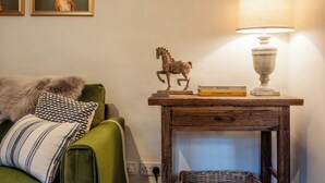 A cozy living room with a green sofa, a small wooden table with a lamp, and a decorative horse figurine. - Beautiful 2 BD Cottage in the Cotswolds (Moreton-in-Marsh)