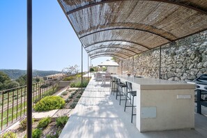 An outdoor bar area with a stone wall backdrop, a pergola providing shade, and a view of the landscape. - CAN CABELLUT - Villa with private pool and mountain views - Free WiFi (Puigpunyent)