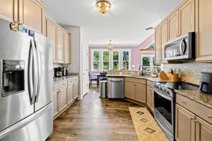 A modern kitchen with stainless steel appliances, wooden cabinets, and a view of the outdoors through large windows. - Lakefront Luxury - Beach, Dock, Deck @ Lake Anna (Mineral)