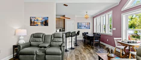 A living room with a sectional sofa, a dining area with a table and chairs, and a kitchen in the background.