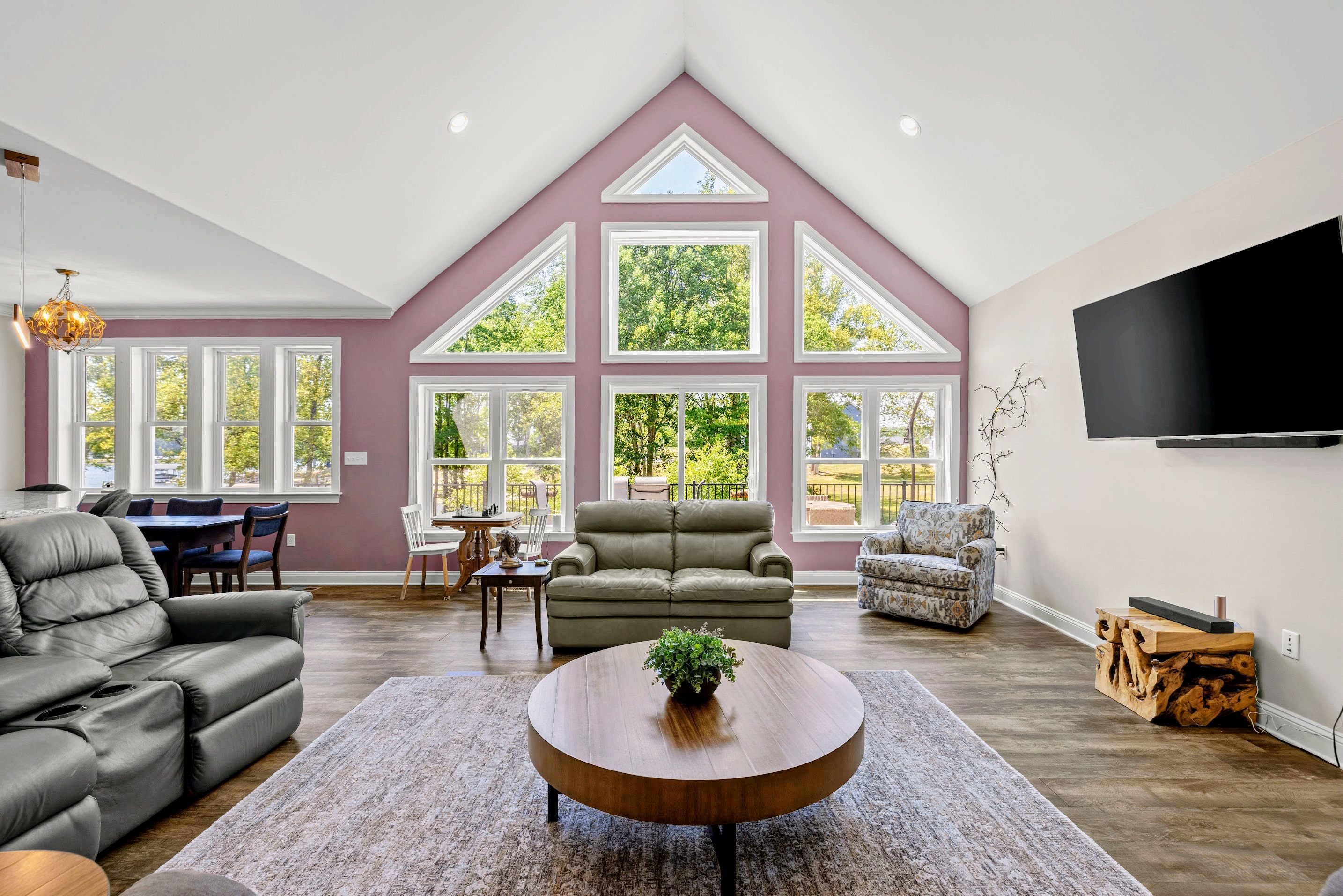 Un salon spacieux doté d’un haut plafond, de grandes fenêtres, d’un téléviseur à écran plat fixé au mur et de différents types de sièges, notamment un canapé et des fauteuils.
