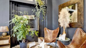 A modern living room with a dark wall, a round wooden coffee table, leather chairs, a potted plant, and a mirror. - Bohome Reserve:  Chicago Wicker Park • Sauna • Chef's Kitchen • Outdoor Lounging (Chicago)