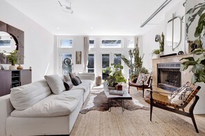 A modern living room with a white sofa, a coffee table, a fireplace, and large windows. - Bohome Reserve:  Chicago Wicker Park • Sauna • Chef's Kitchen • Outdoor Lounging (Chicago)