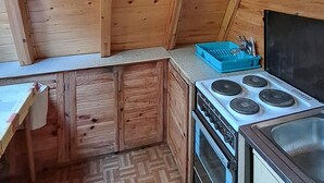 Una cocina pequeña con armarios de madera, una estufa y un recipiente azul para utensilios.