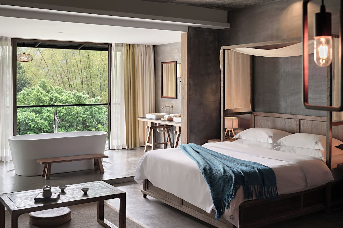 Un dormitorio moderno con una cama grande, una bañera y vistas a zonas verdes.