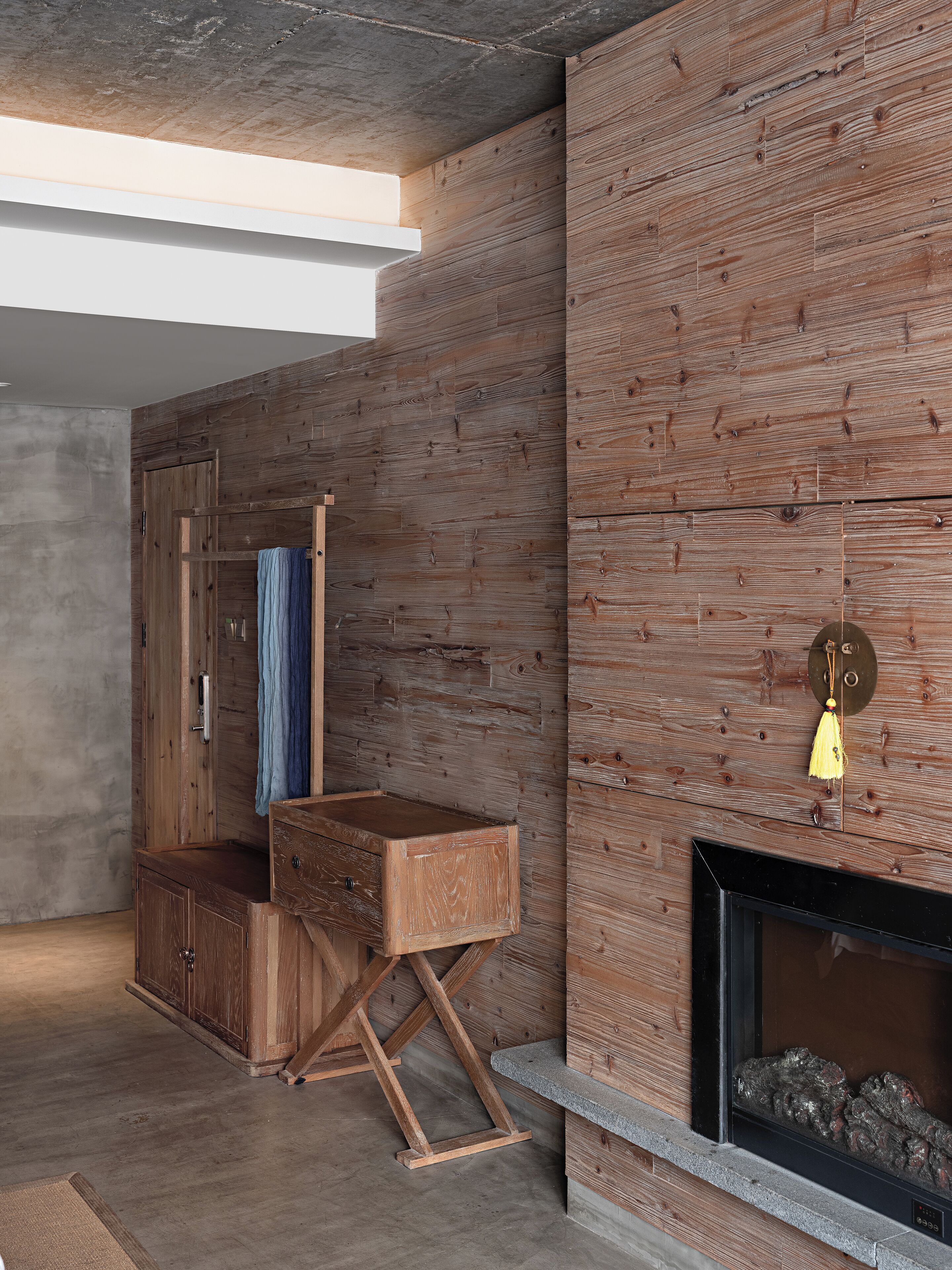 A modern interior with a wooden wall, a built-in bench, a hanging light fixture, and a fireplace.