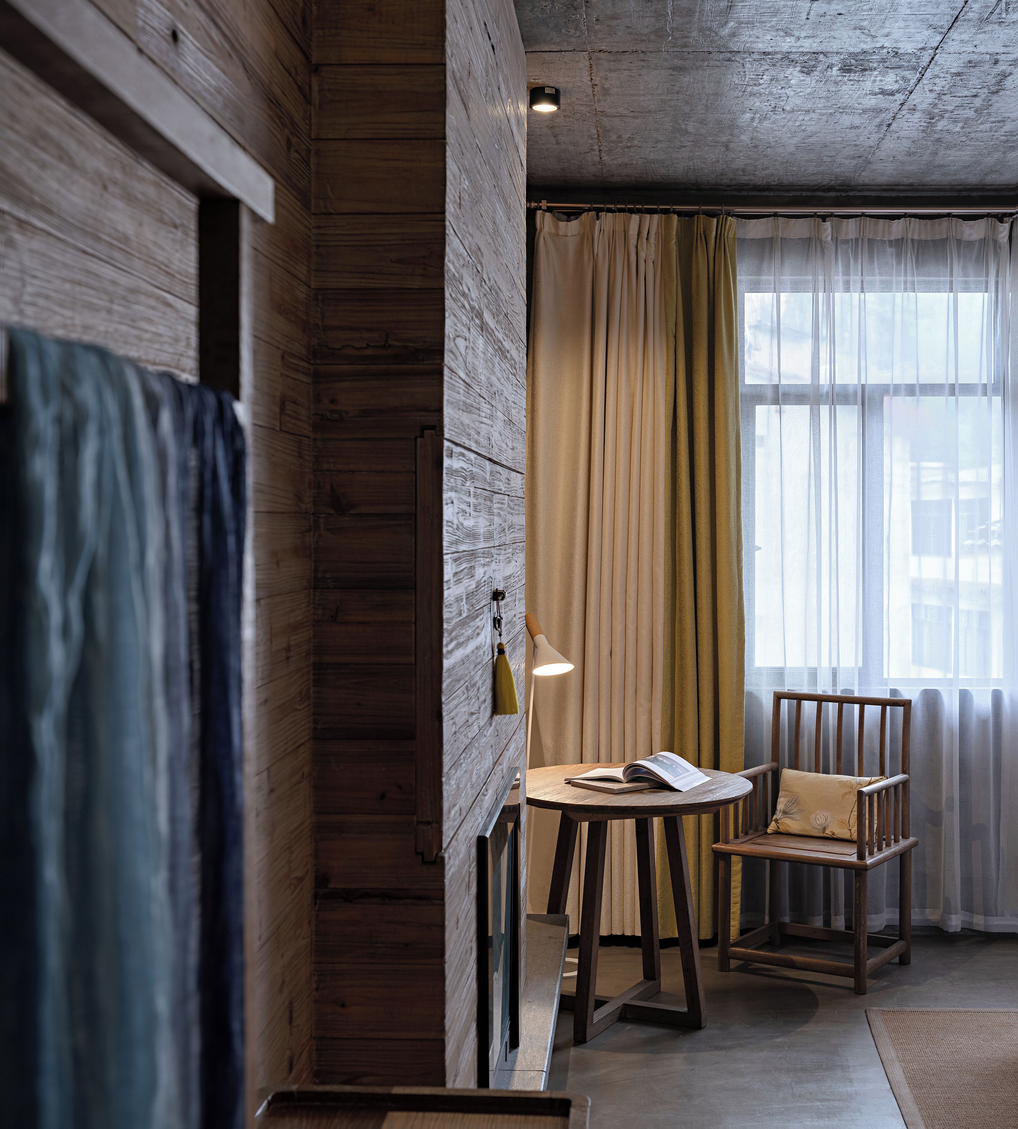 A room with wooden walls, a round table with a book, a chair, and a lamp.