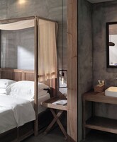 Una cama con dosel, una mesita de noche con espejo y un tocador de madera con lavamanos.