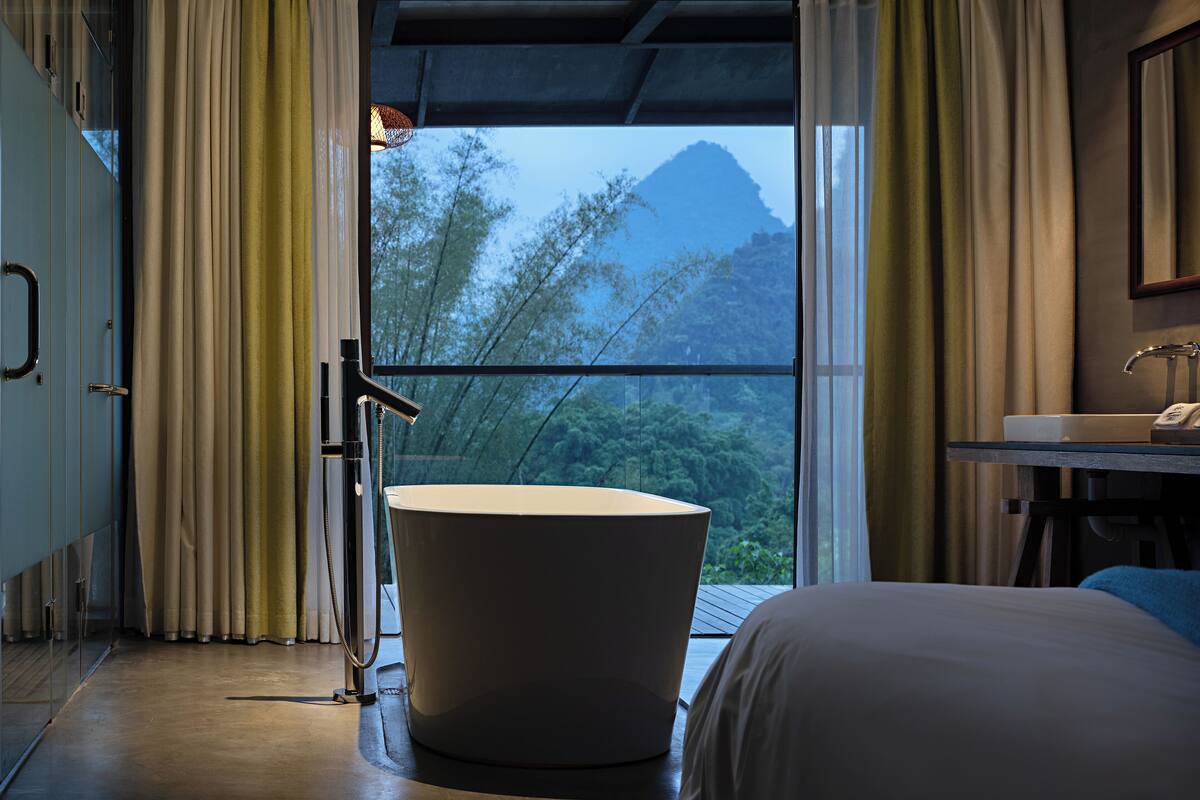 Un baño moderno con bañera, lavamanos y un amplio ventanal con vistas a la montaña.