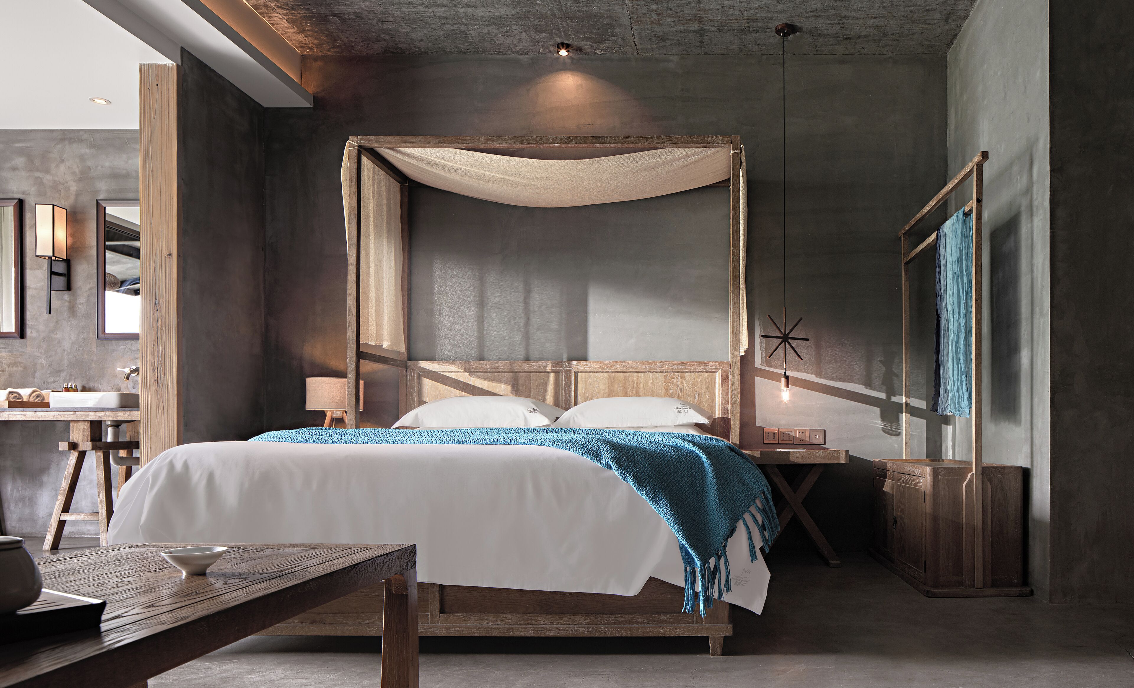 Un dormitorio moderno con una cama con dosel de madera, una mesita de noche con un cuenco y una mesita auxiliar con una lámpara.