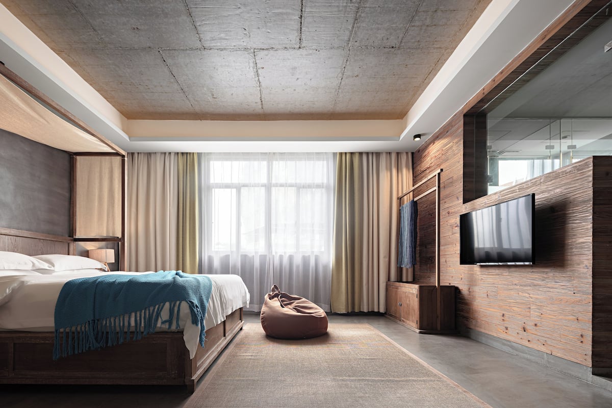 Un dormitorio moderno con cabecera de madera, una cama grande, un sillón de mimbre y un televisor montado en una pared de madera.