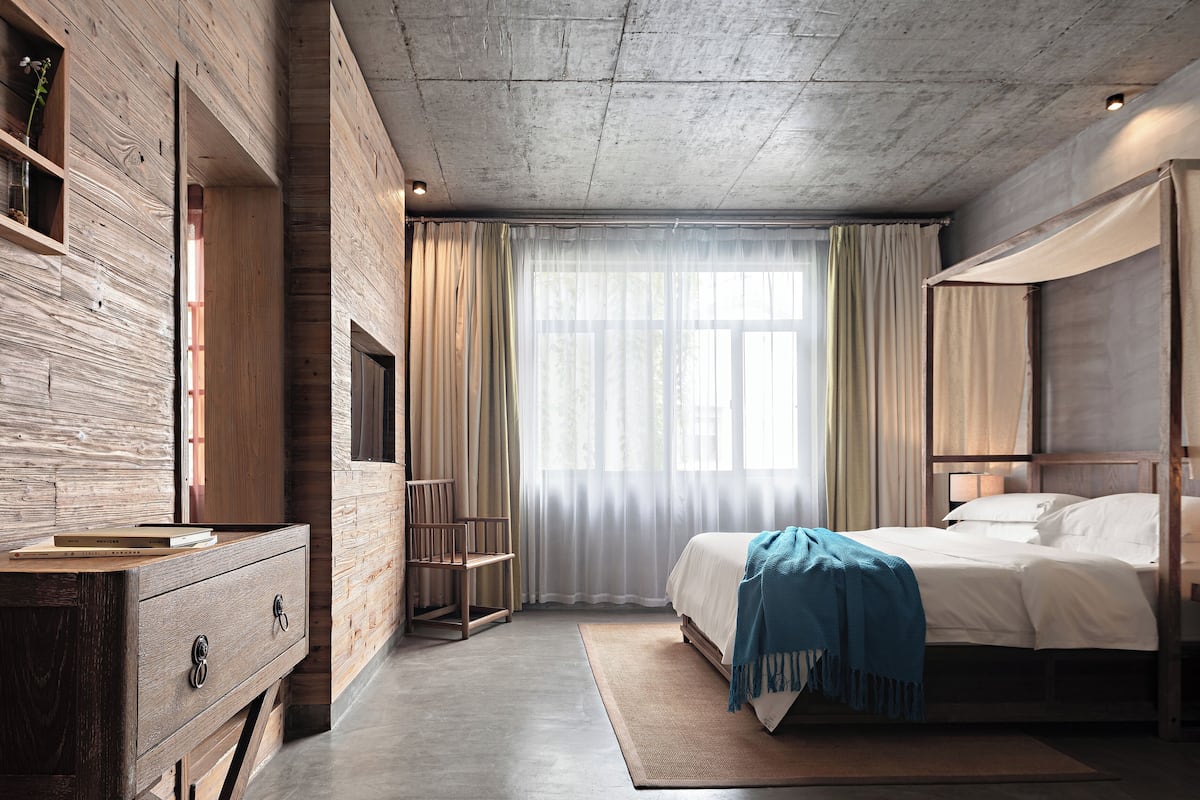 Un dormitorio con pared de madera, una cama con ropa de cama blanca, un plaid azul y una mesita de noche de madera.