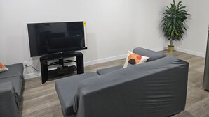 A modern living room with a flat-screen TV on a stand, a grey sofa, a small table, and a potted plant. - Your home away from home—comfortable, and calm. proximity to popular attractions (Edmonton)