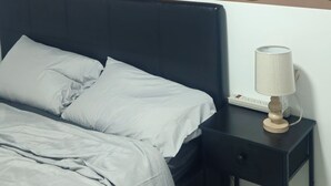 A neatly made bed with grey bedding, a black nightstand with a lamp, and a patterned wall above the bed. - Your home away from home—comfortable, and calm. proximity to popular attractions (Edmonton)