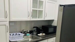 Una cocina con armarios blancos, un refrigerador de acero inoxidable, un microondas y un fregadero.