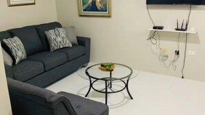 Una sala de estar moderna con un sofá gris oscuro, una mesa de centro redonda y un televisor de pantalla plana montado en la pared.