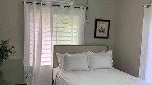 Un dormitorio con cama, cortinas, aire acondicionado, ventilador de techo y un cuadro en la pared.
