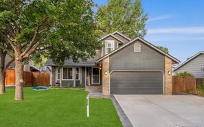 A residential house with a garage, a well-maintained lawn, and a tree. - City Cabin Hideaway w/ Spa, Pool Table & Arcade (Greeley)