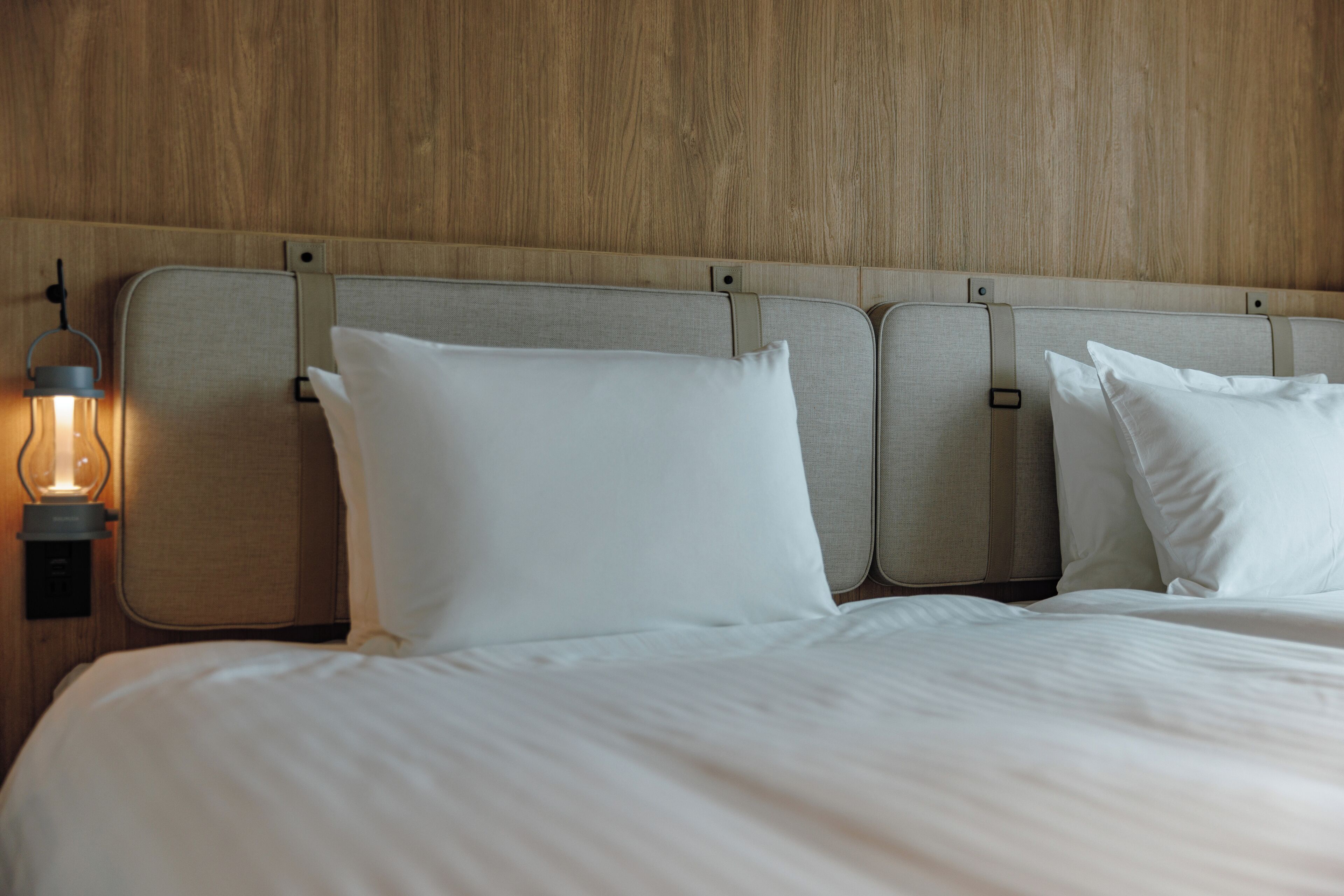 Een bed met wit beddengoed, een hoofdbord met een lamp en een houten wand.