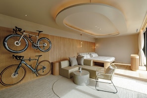 Een moderne hotelkamer met een bank, een klein rond tafeltje, een rieten stoel, en twee fietsen aan de muur bevestigd.