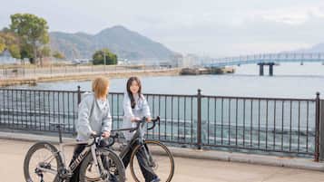 Dos personas en bicicleta junto a una orilla con un puente al fondo.