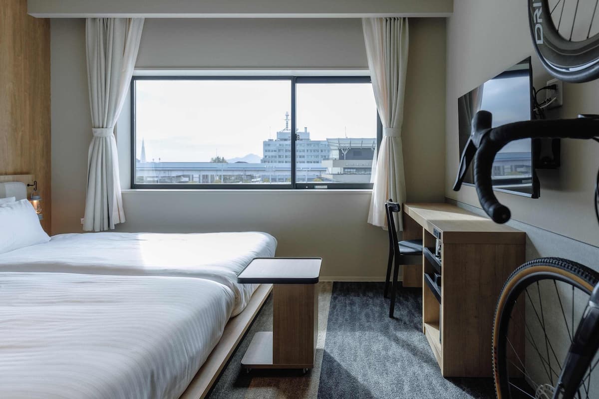 Une chambre d’hôtel avec un lit, un bureau, un vélo et une vue sur la ville.