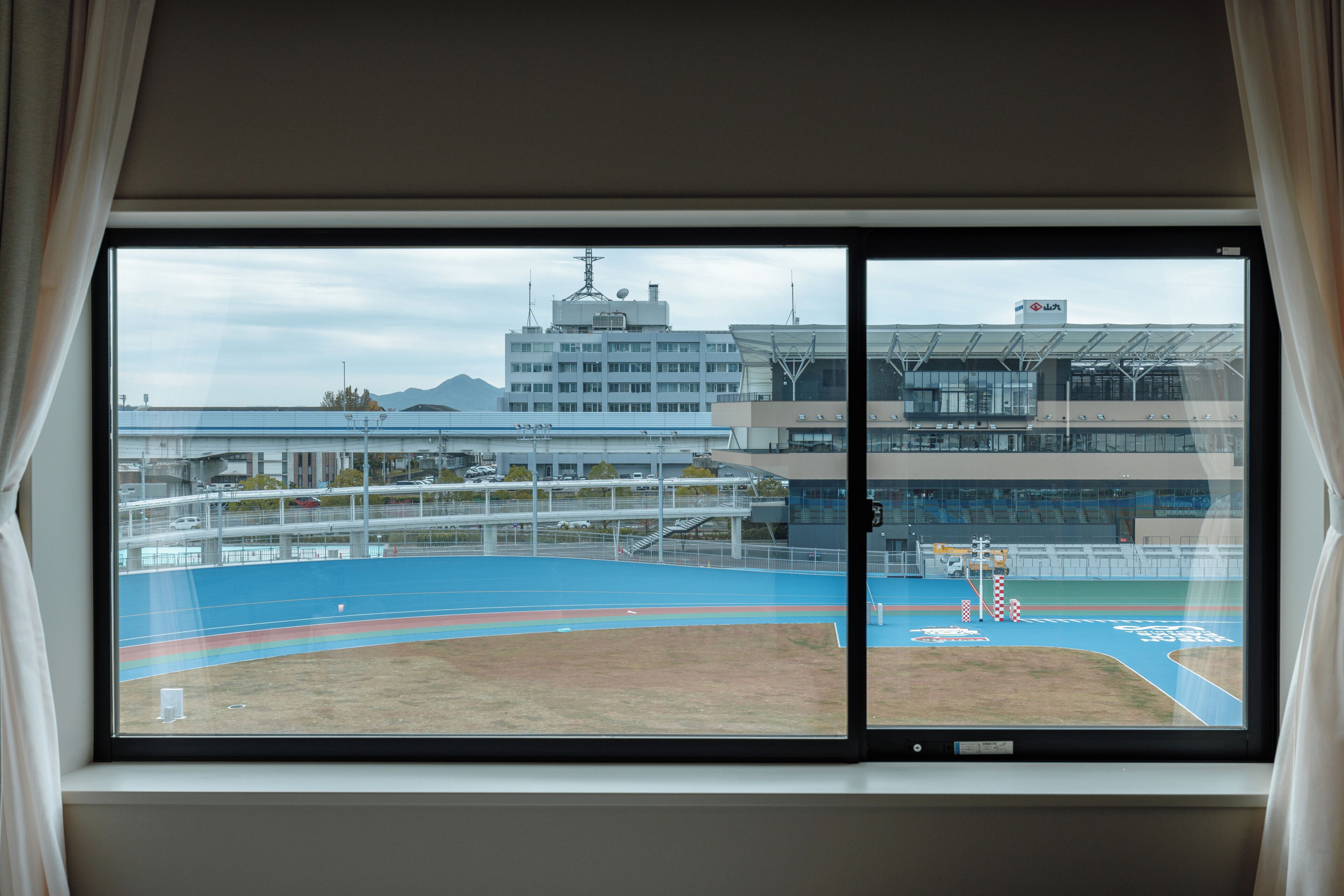 A window view of a sports field with a building in the background.