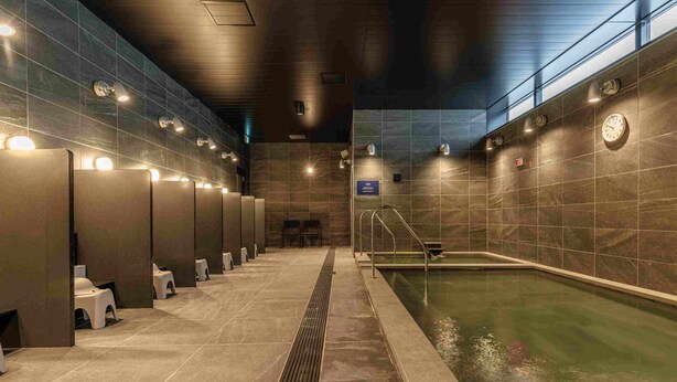 Un espace piscine intérieur moderne, doté de cabines de change individuelles, d’une piscine centrale et d’une horloge au mur.