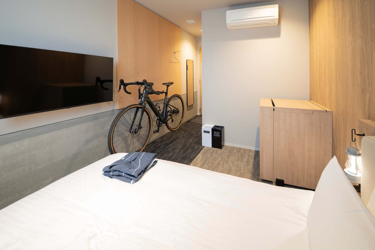 Une chambre d’hôtel avec un lit, un vélo, une télévision, un miroir et une armoire.