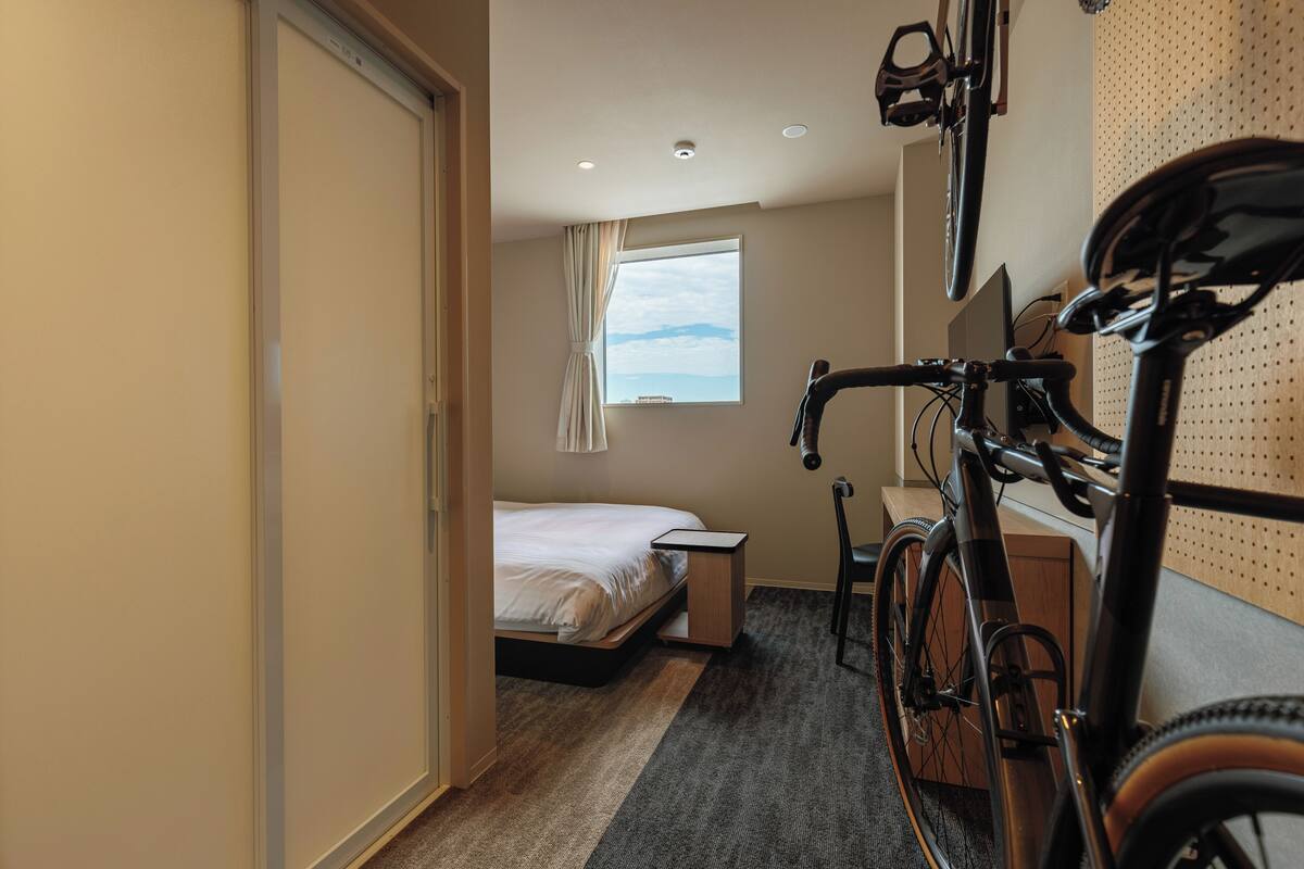 Une chambre d’hôtel avec un lit, un bureau, un vélo et une fenêtre donnant sur un beau paysage.