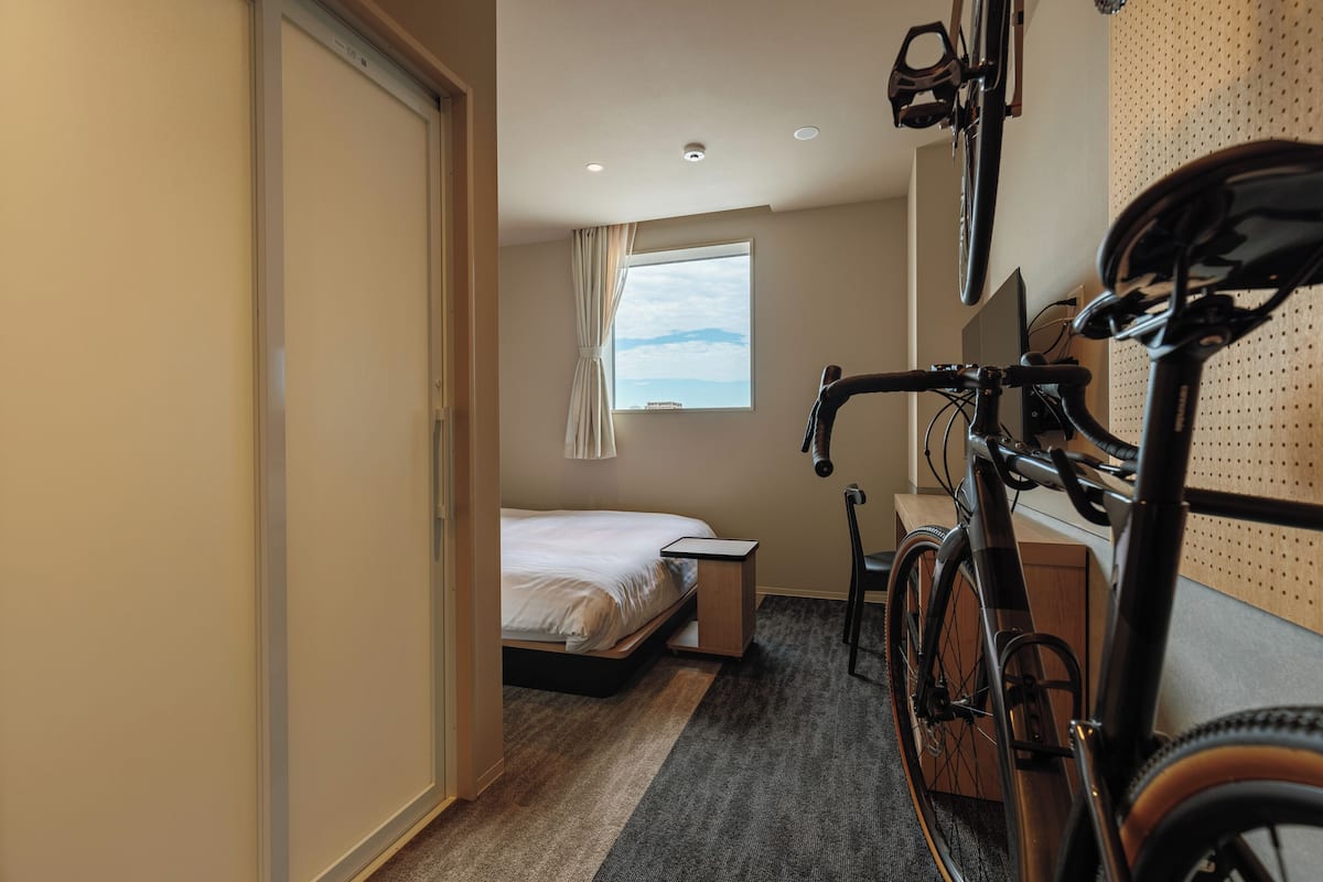 Habitación de hotel con cama, escritorio, bicicleta y ventana con vistas.