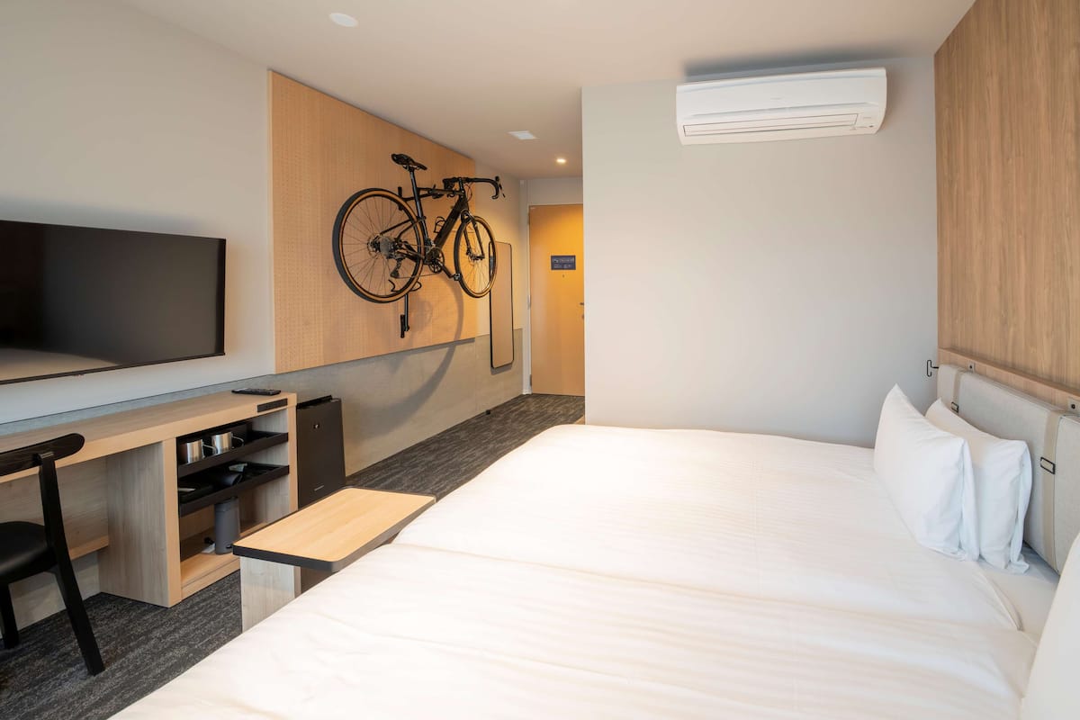 Une chambre d’hôtel comprenant un lit, un bureau avec une chaise, un vélo fixé au mur, une télévision et un appareil de climatisation.