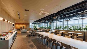 Une cafétéria moderne avec de longues tables et des chaises, un espace buffet et de grandes fenêtres donnant sur le paysage urbain.