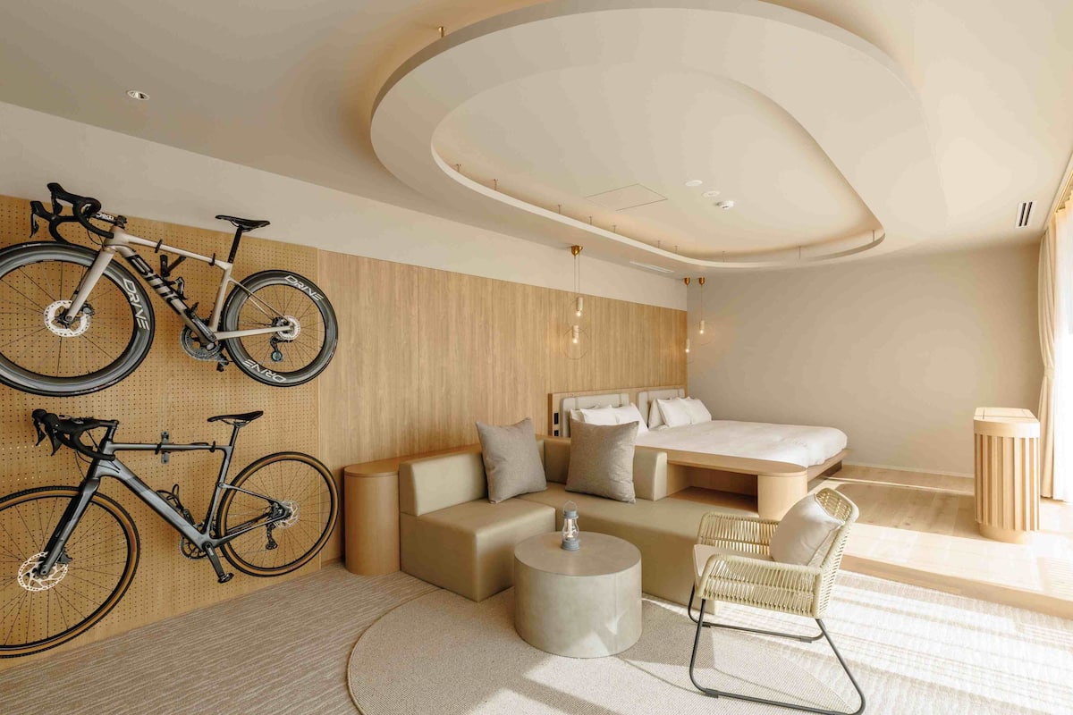 Une chambre d'hôtel moderne avec un canapé, une table basse ronde, un lit et des vélos fixés au mur.