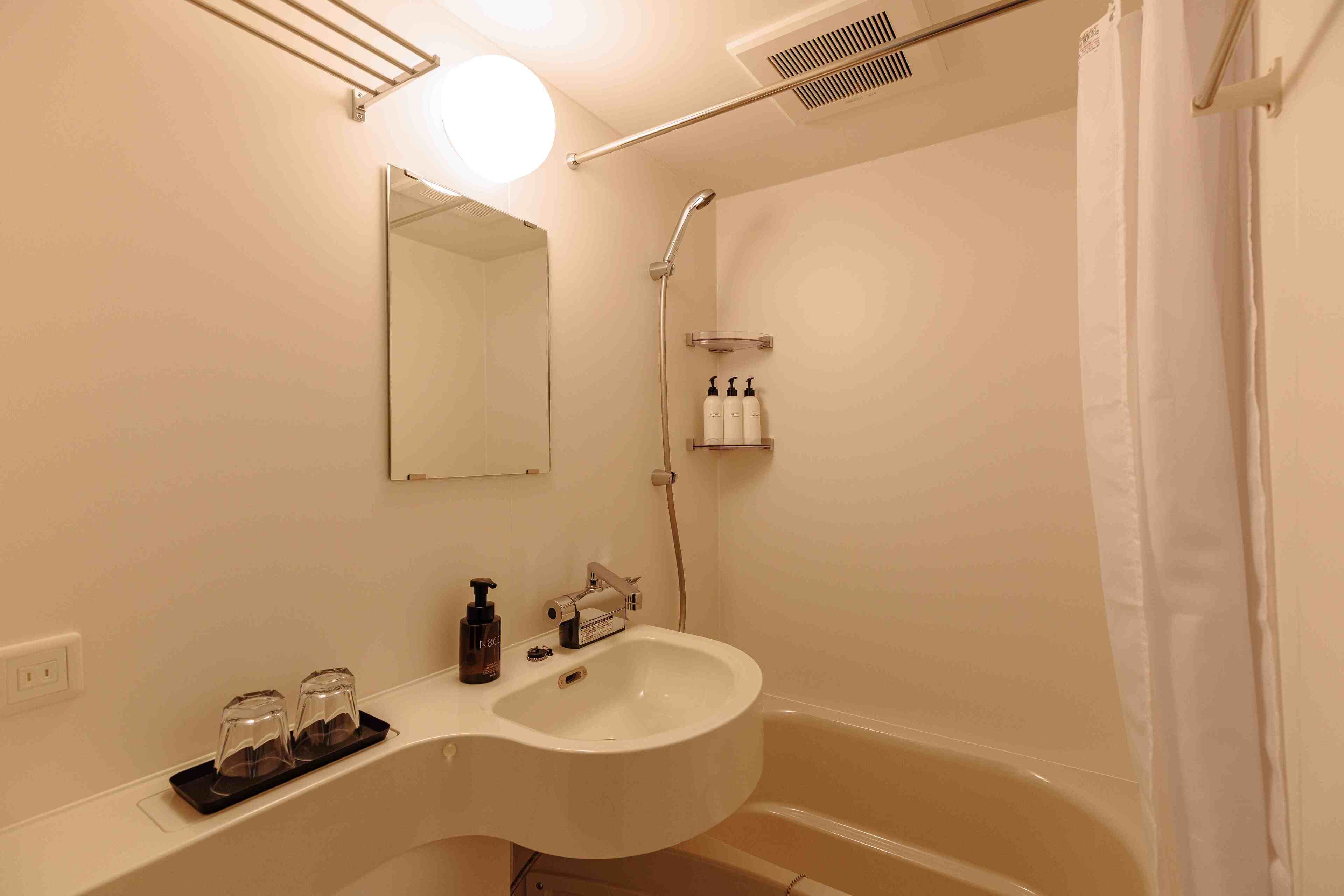 A bathroom with a white sink, a mirror, a shower, and a towel rack.