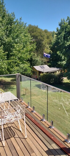 A wooden deck with a glass railing, a metal chair, and a flagpole with an Australian flag. - JAMIESON RIVERFRONT PROPERTY WITH FANTASIC OUTDOOR ENTERTAINMENT AREA (Jamieson)
