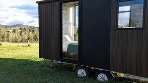 A modern, compact mobile home with a large sliding door revealing a bedroom with a bed and a green blanket. - Pasture and Paws by Tiny Away (Shannon Brook)