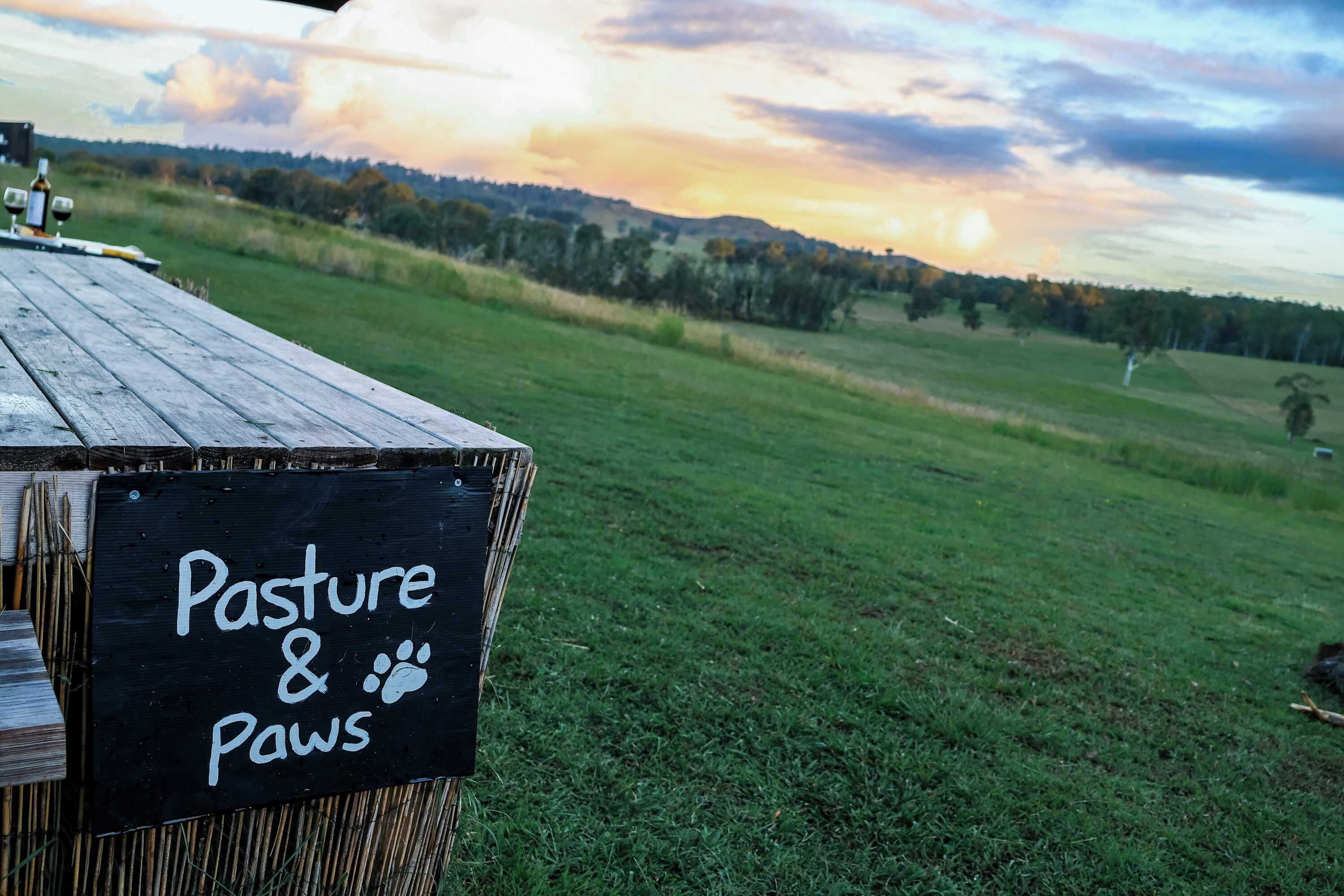 A sign reading 'Pasture & Paws' on a wooden structure.