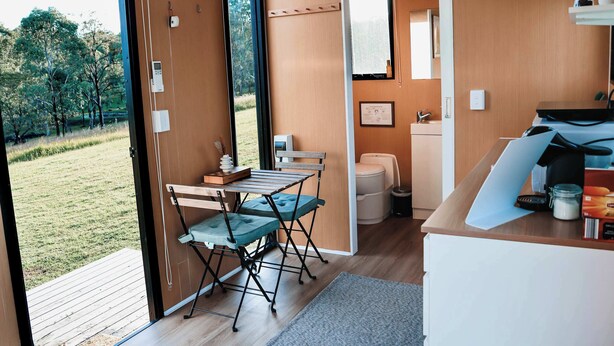 A modern kitchen with a wooden countertop, a dining area with a table and chairs, and a view of a grassy area through an open door. - Pasture and Paws by Tiny Away (Shannon Brook)