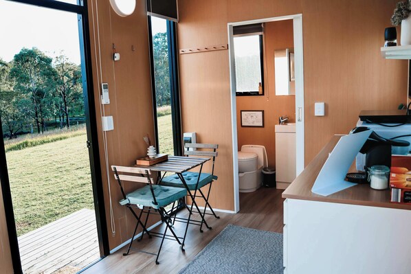 Una cocina moderna con encimera de madera, un comedor con mesa y sillas, y vista a un área verde a través de una puerta abierta.