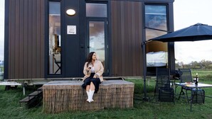 A modern cabin with a wooden exterior, a covered outdoor seating area, and a visible entrance. - Pasture and Paws by Tiny Away (Shannon Brook)