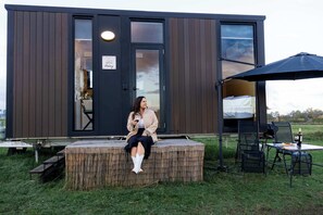 Una cabaña moderna con fachada de madera, un espacio cubierto para sentarse al aire libre y una entrada visible.