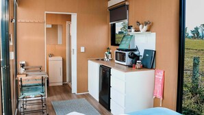 A compact room with a kitchenette, a bed, a small table, and a window with a view of the outdoors. - Pasture and Paws by Tiny Away (Shannon Brook)